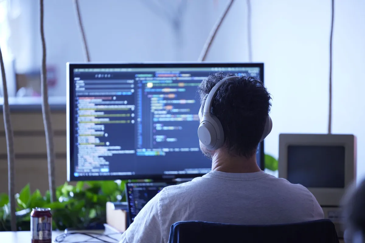 Headphones on, a developer stares at his monitor, intently working on some code.