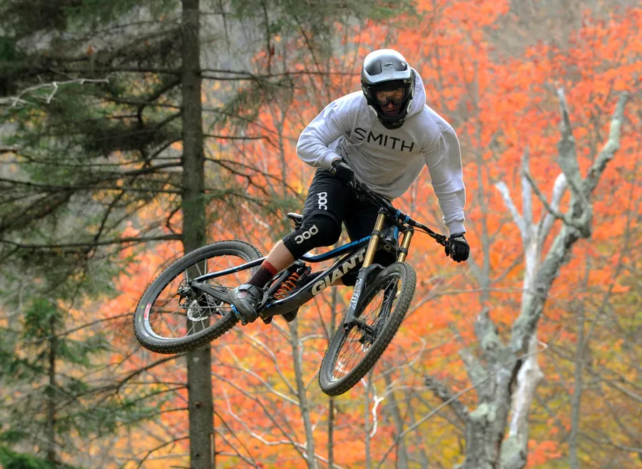 Mountain biker jumps airborne on bike with autumn trees in the background.